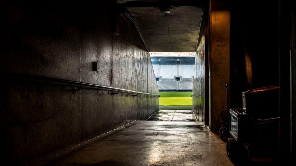An empty stadium tunnel opens toward a bright football field.