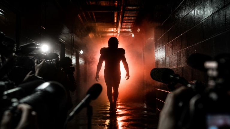 An anonymous football player approaches reporters in a dark stadium corridor.